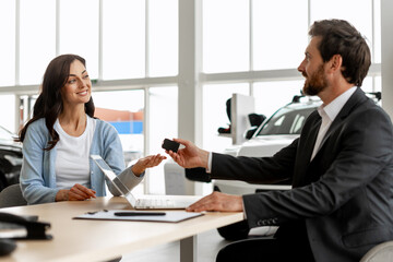 Car salesman giving car keys to a woman at the dealership
