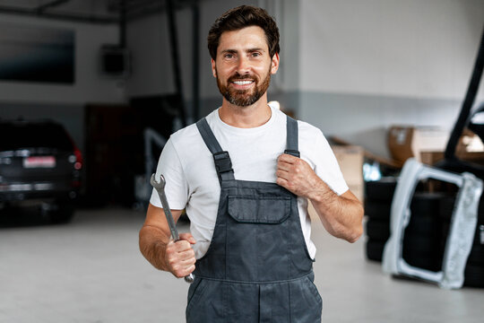 Confident mechanic holding wrench and smiling in auto repair shop