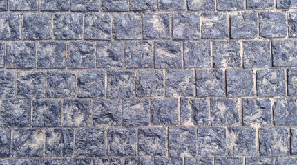 Textured stone pavement made of square blue-grey granite blocks arranged in grid pattern. Top view...
