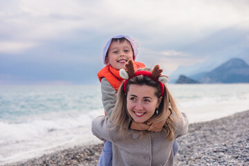A mother and her young son play on a winter beach. The mother has long blond hair and wears a...