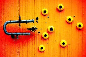 Rusty metal latch on vibrant orange surface with yellow circular holes