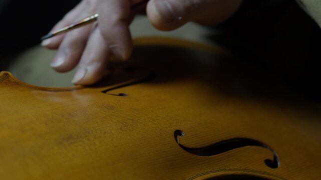 Hands of a luthier precisely darkening violin edges, simulating natural wear and aging on the handcrafted instrument on edges and purfling, with finger and paintbrush traditional tecqnique - Powered by Adobe