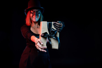 Young woman wearing black costume and hat, holds gift on black background. Concept halloween gifts, holiday sales, halloween party, black friday.
