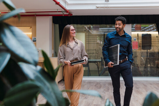Businessman with solar panel and businesswoman with digital tablet walking in office