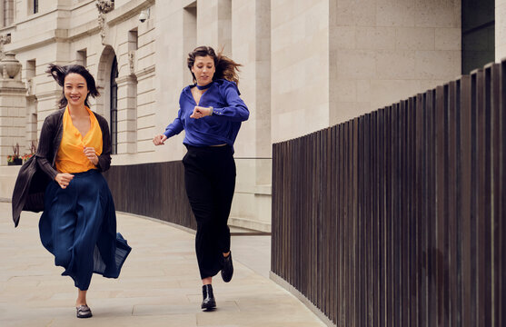 Businesswoman with colleague checking time and running on footpath
