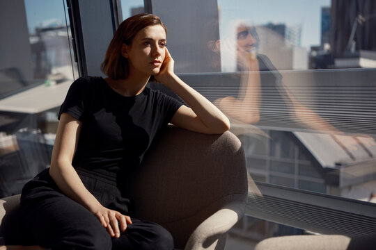 Thoughtful young businesswoman sitting on chair near window at office
