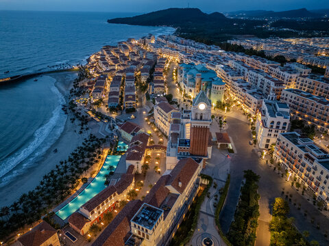 Aerial view of a coastal town with vibrant lights illuminating the clock tower and beachfront buildings, contrasting with the dark sea, Phu Quoc, Kien Giang, Vietnam.