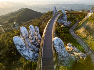 Aerial view of Golden Bridge held by giant stone hands amidst lush hills, Ba Na Hills, DaNang, Da Nang, Vietnam.