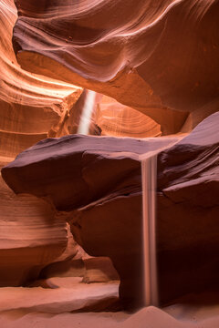 A beam of light shines through the red rock formations of Antelope Canyon, creating a stunning visual effect as it illuminates the sandy floor below.