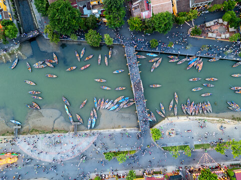 Aerial view of a river crowded with boats and people, with a bridge connecting bustling banks, creating a vibrant tapestry of color and movement, H&aacute;&raquo;&trade;i An, Qu&aacute;&ordm;&pound;ng Nam, Vietnam.