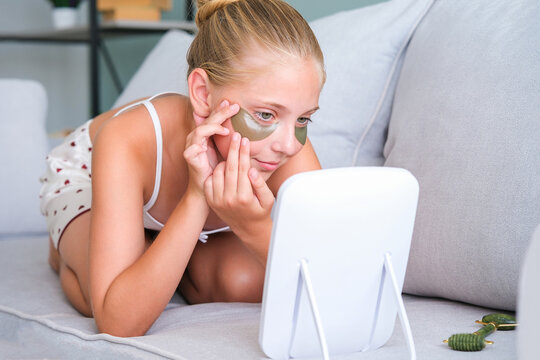 The girl looks in the mirror. The teenager put gel  patches under her eyes.