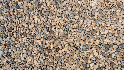 Detailed full frame view of natural pebbles and small stones creating a rustic and earthy textured background. Versatile for nature outdoor or abstract design elements.