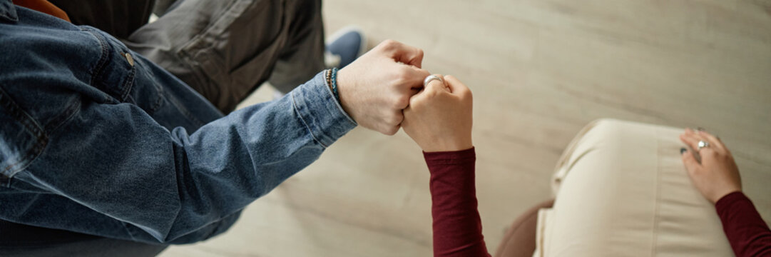 Teenagers sitting together during counseling session, boy and girl giving fist bump, hands and partial arms visible, demonstrating support and connection - Powered by Adobe