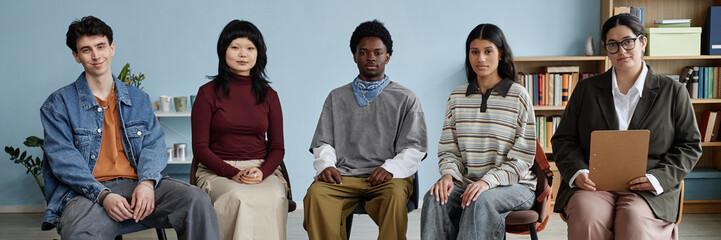 Group of multiethnic teenagers sitting in counseling session with young female counselor holding...