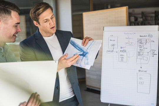 Businessman explaining wind turbine drawing to colleague in office