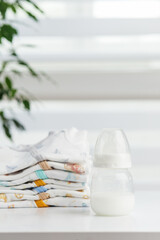 Baby bottle with folded clothes on table. Baby care.