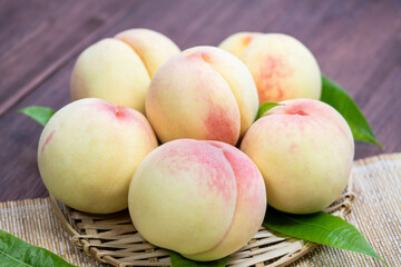 White Peaches with leaves on the wooden table, Fresh White Peach on wooden basket in wooden Background.