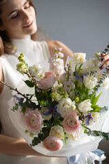 Young caucasian female holding elegant bouquet of pastel flowers in white dress
