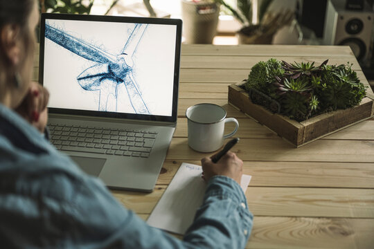 Freelancer writing notes with wind turbine sketch on laptop screen at home