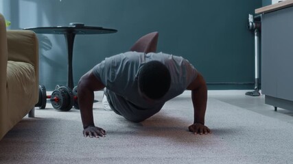 Ground level shot of sporty African American man doing push-ups while working out at home alone cultivating willpower, strength and self-discipline - Powered by Adobe
