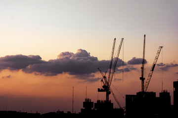 Construction crane on building surrounded by high rise buildings in the middle of the capital with blue sky at sunset. Concept of industry, construction area, development of business district.