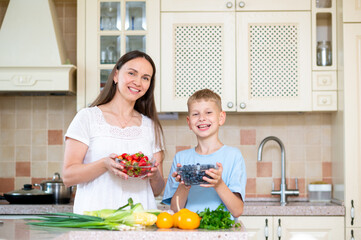 Healthy family moment: mom and teenage son with fresh berries in bright kitchen