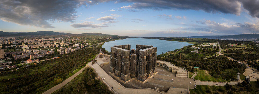 Aerial view of the Chronicles of Georgia monument standing boldly against the tranquil blue reservoir and the sprawling city, Tbilisi, Tbilisi, Georgia.