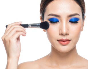 A woman with vibrant blue eyeshadow is applying makeup on her cheek using a large makeup brush with her eyes closed.