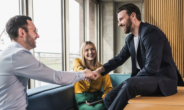 Happy business colleagues bumping fists sitting at office