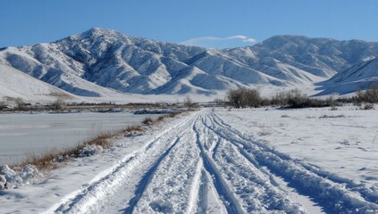 Winter landscape with snowy mountain backdrop and clear trail leading through the snow. Partially frozen water body on the left. Tracks guide the eye toward the horizon