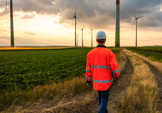 Engineer in reflective clothing walking towards wind turbines