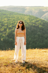 A stylish young woman stands confidently in a sunlit field, fully embracing the beauty of nature and fashion
