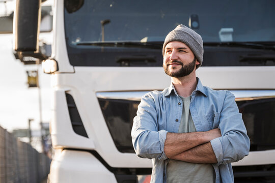 Smiling truck driver wearing knit hat standing in front of truck
