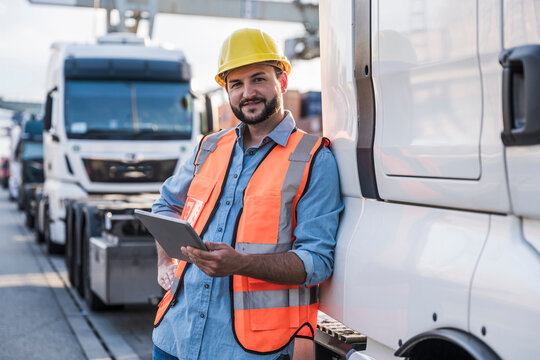 Happy truck driver leaning on truck with tablet PC