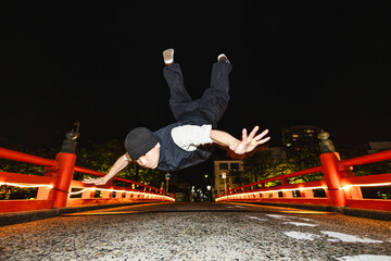 ライトアップされた和風の橋でブレイクダンスジャンプを披露する若い男性