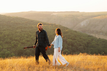 A joyful couple enjoys a peaceful evening walk through the beautiful nature, hand in hand, during a stunning sunset