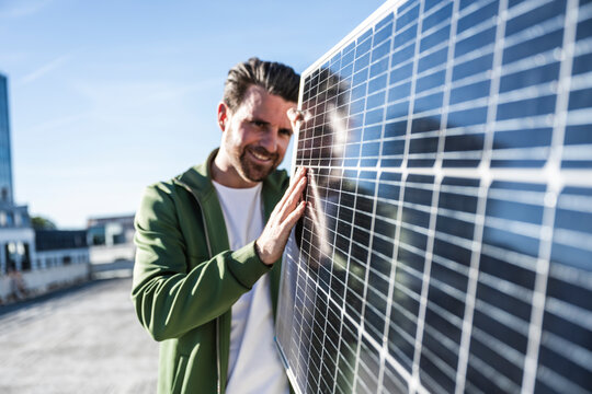 Smiling engineer examining solar panel on sunny day