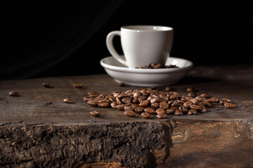 Low key image of a white coffee cup surrounded by scattered coffee beans
