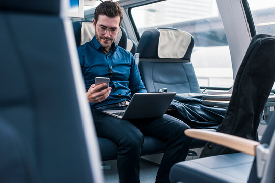 Businessman sitting with laptop and using smart phone in train