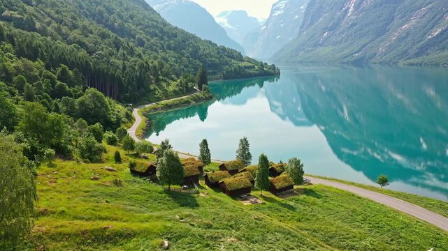 Aerial view of cabins with grass roofs nestled by a serene lake reflecting the mountains in a tranquil scene, Breng seter, Vestland, Norway.