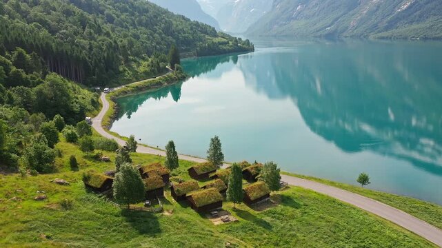 Aerial view of Lodalsvatnet lake mirroring the majestic mountains, contrasting with the green roofed cabins beside the road, Loen, Vestland, Norway.