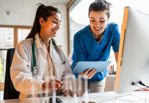 Happy nurse sharing tablet PC with female doctor in medical clinic