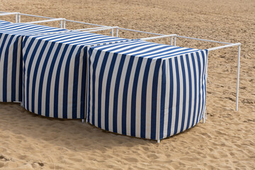 Cabines de plage rayées à l'ombre sur le sable fin d'une station balnéaire.