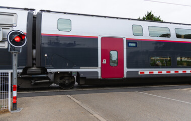 Train à double niveau passant un passage à niveau avec un eu rouge en milieu urbain sur une route française.