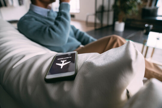 Flight mode symbol on mobile phone by man sitting on sofa at home