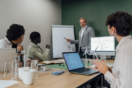 Mature businessman explaining on flipchart to colleagues in office