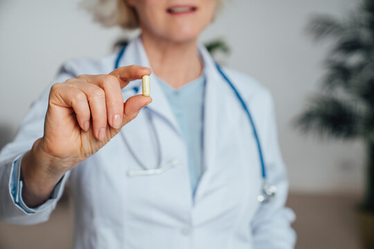Mature doctor showing capsule pill at clinic