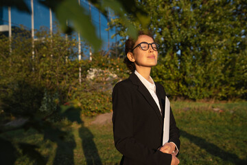 Businesswoman standing with file folder and eyes closed in office park