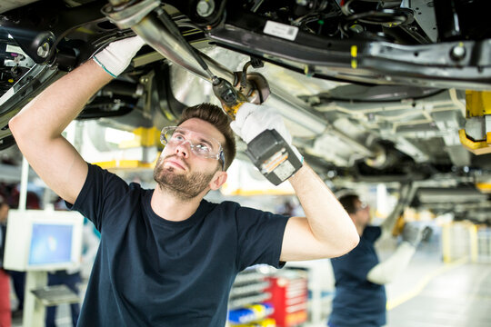 Two colleagues working at car underbody in modern factory