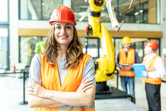 Confident industrial worker standing in robotic factory with arms crossed